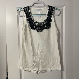White sleeveless top with black neckline.